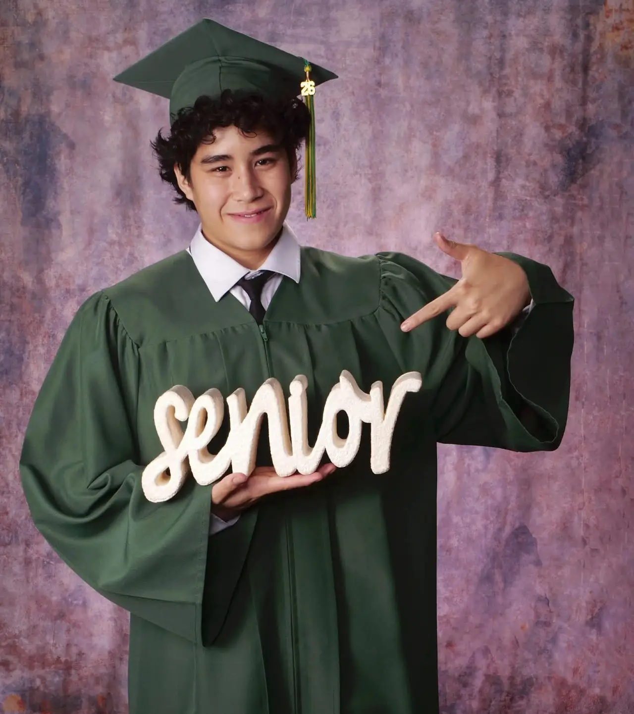 Elan in his green graduation cap and gown holding a senior sign