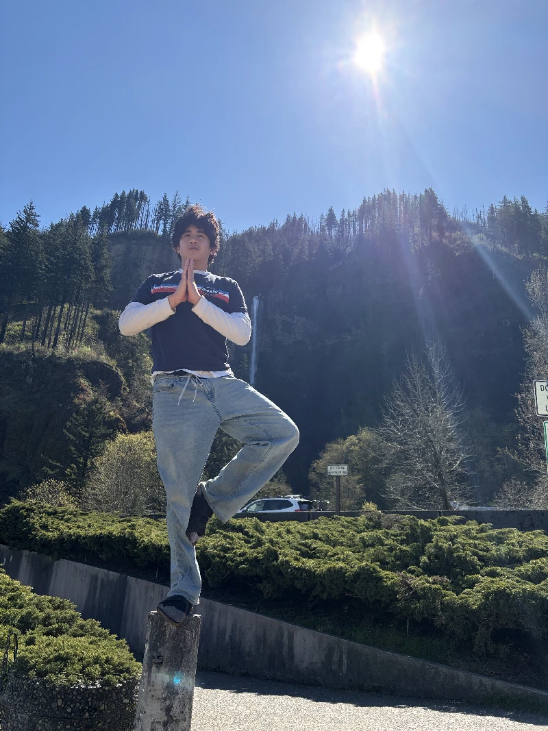 Elan balancing in a yoga tree pose in front of a forest waterfall